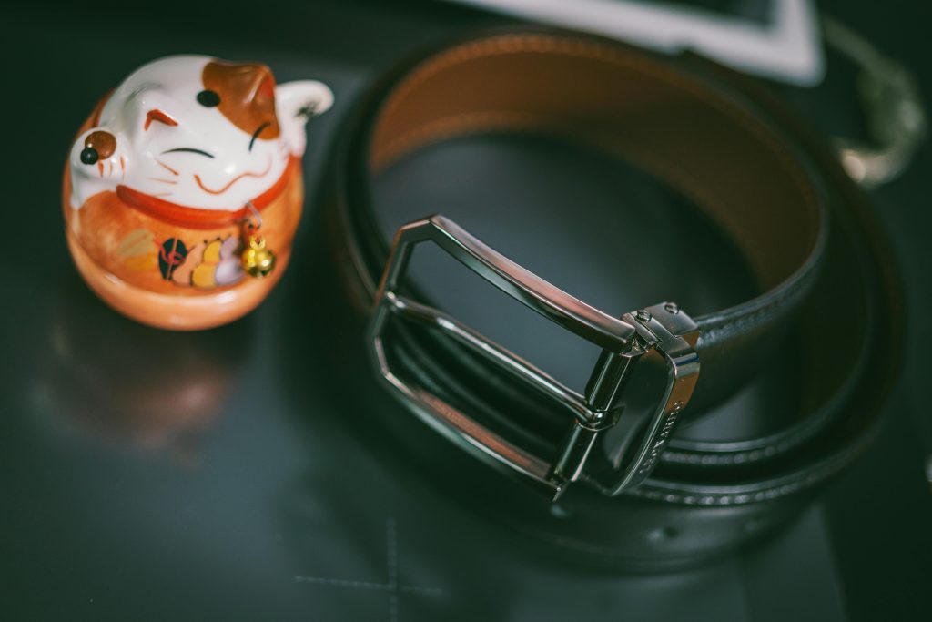 Elegant black leather belt beside a traditional Japanese maneki-neko, symbolizing luck and fortune.